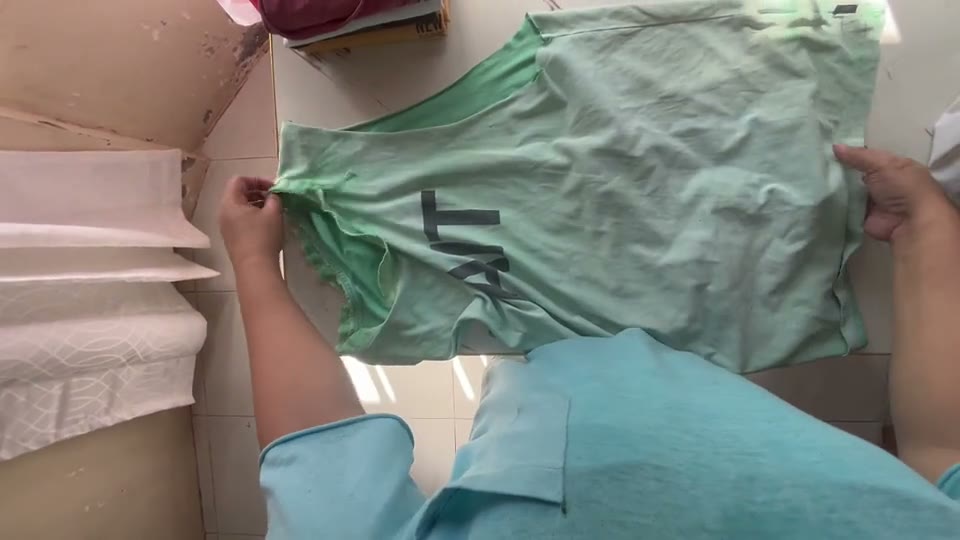 First-person view of two hands folding a green shirt.